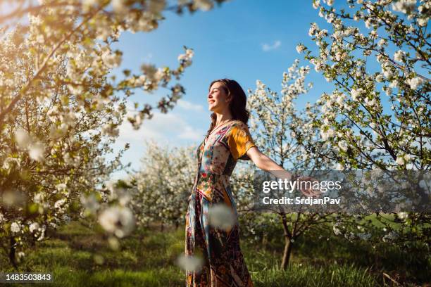 mujer joven disfrutando de un día de primavera sin preocupaciones en un huerto floreciente - abril fotografías e imágenes de stock