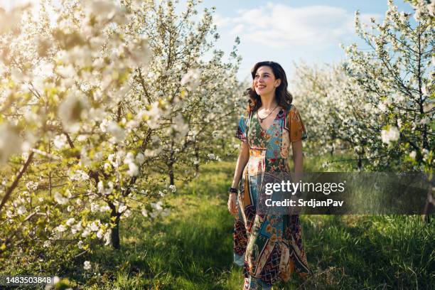 beautiful young woman walking through blossoming orchard in spring - april 22 stock pictures, royalty-free photos & images