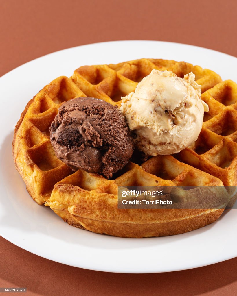 Two scoops of chocolate and caramel ice cream on belgian waffle, Close-Up, Brown background