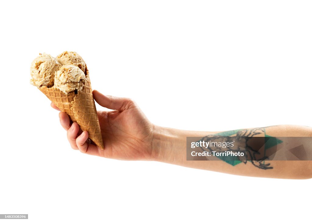 Scoop of caramel and nut ice cream in homemade waffle ice cream cone in hand isolated on white