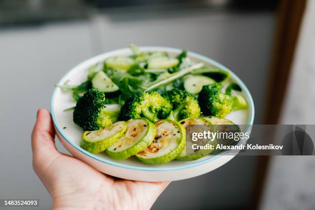 woman hand's holding healthy green vegan salad with broccoli, zucchini, cucumber and arugula. healthy and detox food concept. - leaf vegetable stock-fotos und bilder