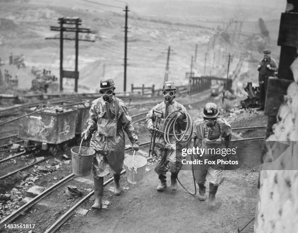 Lancashire coal miners wearing protective clothing, gas masks and carrying fire fighting stirrup pump hoses and buckets during an ARP training...