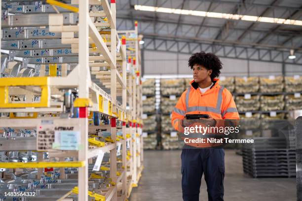 optimize and improve your automotive parts warehouse for efficiency and growth. a male african american warehouse worker using a tablet computer in a factory warehouse to verifying of chassis parts on pallets. - pezzo di ricambio foto e immagini stock