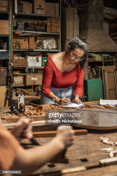 mujer tomando notas mientras trabaja en un banco en un estudio de carpintería - fabricantes de muebles de artesania fotografías e imágenes de stock