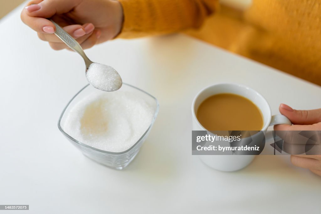 Mão está derramando açúcar para xícara de café