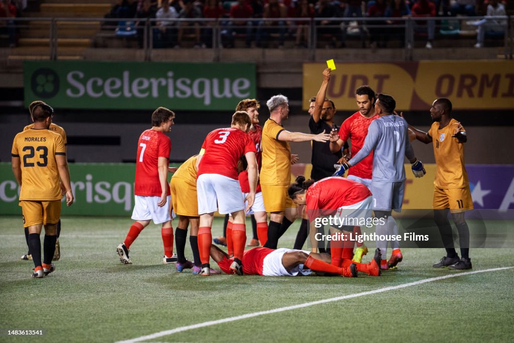 Teammates surround an injured soccer player as the referee gives yellow card during international competition