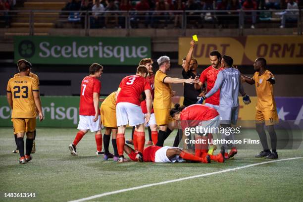 teammates surround an injured soccer player as the referee gives yellow card during international competition - referee card stock pictures, royalty-free photos & images