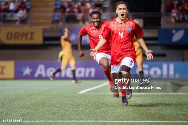 elated male soccer player runs with his arms outstretched while cheering in celebration of scoring a goal - middenvelder voetballer stockfoto's en -beelden