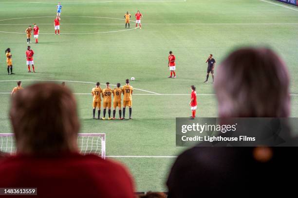 over the shoulder shot of spectators watching as players form a free kick wall attempting to block opponent - stadium seating stock pictures, royalty-free photos & images