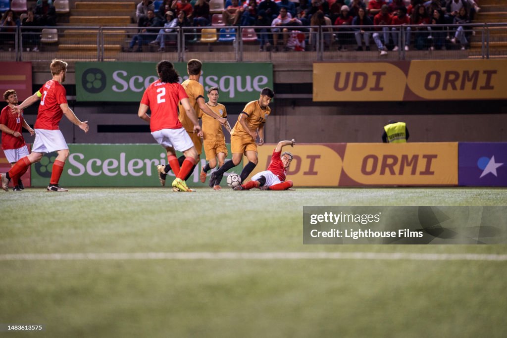 Soccer player slide tackles on the field to steal ball from the opposing team during intense professional match