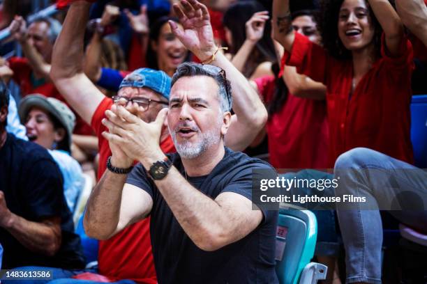 thrilled soccer fans excitedly clap and cheer sitting next to each other in the stadium bleachers - mens world championship stock-fotos und bilder