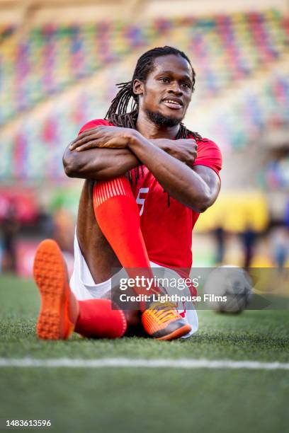 content professional soccer player smiles and stretches as he sits on field before game - middenvelder voetballer stockfoto's en -beelden