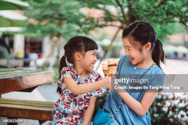 lovely cheerful sister cheersing with their ice-cream cones while playing in park - gefrierkost stock-fotos und bilder