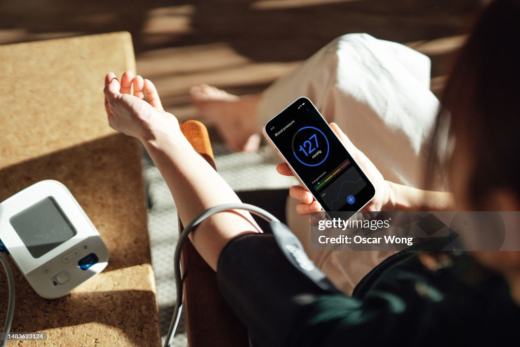 Elevated view of woman checking her blood pressure with a blood pressure monitor and mobile app on smartphone