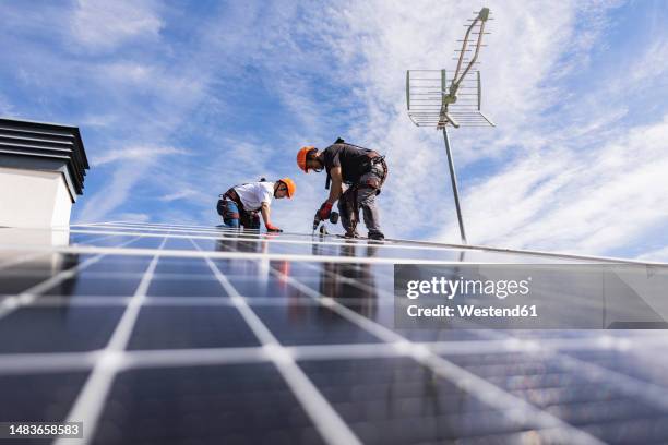 technician with colleague using drill on solar panel - house builder stock-fotos und bilder