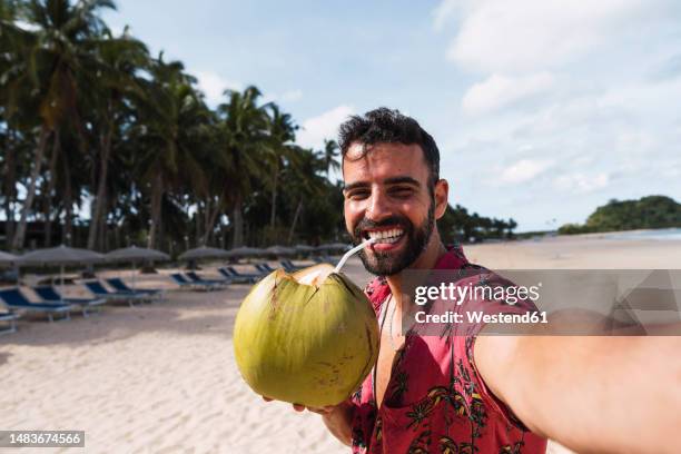 happy man drinking coconut water taking selfie at beach - coconut water stock pictures, royalty-free photos & images