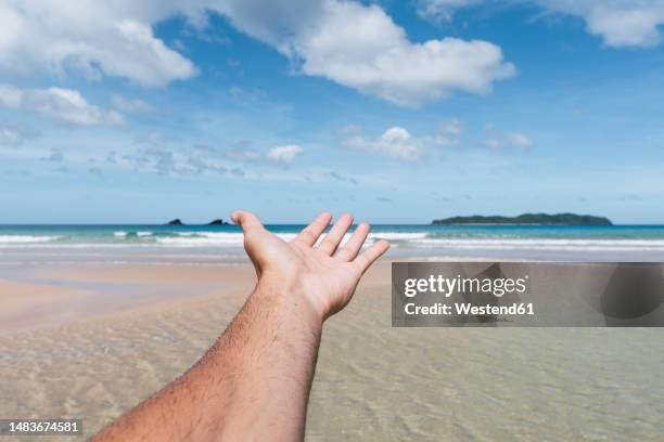 man's hand reaching towards sea at beach - palawan stock-fotos und bilder