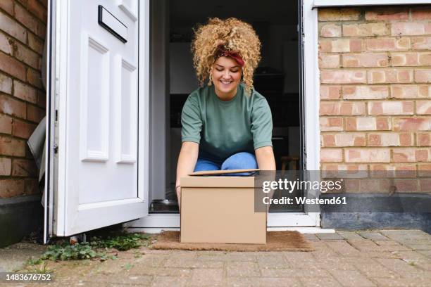 happy young woman picking up packages from doorway - umbral fotografías e imágenes de stock