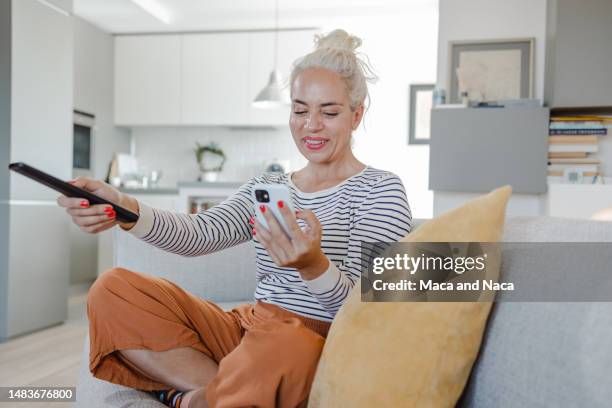 smiling mature woman watching tv at home - glee tv program stockfoto's en -beelden