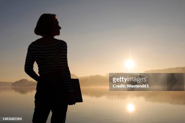 silhouette of freelancer standing with laptop in front of lake - white collar worker dawn light stock pictures, royalty-free photos & images