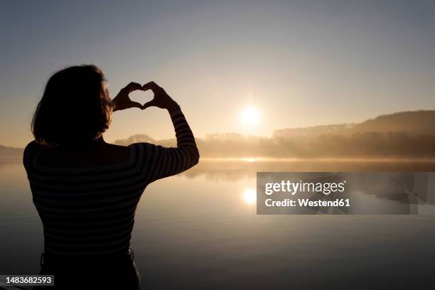 woman making heart shape gesture in front of lake - senior essen stock pictures, royalty-free photos & images