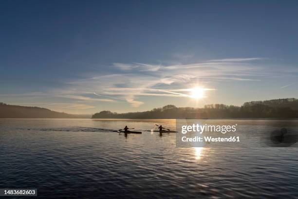 silhouette of canoeists paddling in lake at sunrise - essen sport stock pictures, royalty-free photos & images