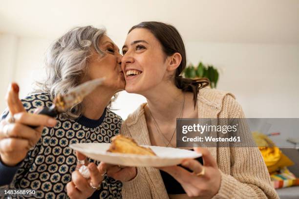 mother serving cake and kissing daughter at home - milestone stock-fotos und bilder