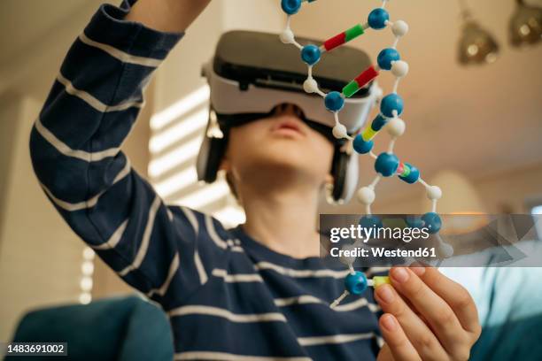 boy examining dna model through vr glasses at home - home base stockfoto's en -beelden