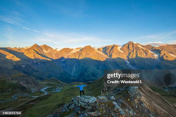 austria, salzburger land, grossglockner road seen from summit of edelweissspitze mountain at dawn with tourist standing with raised arms in foreground - hohe tauern stock pictures, royalty-free photos & images