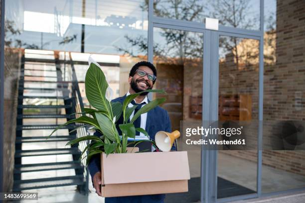 happy businessman with carrying box with office supplies in front of glass wall - umstrukturierung stock-fotos und bilder