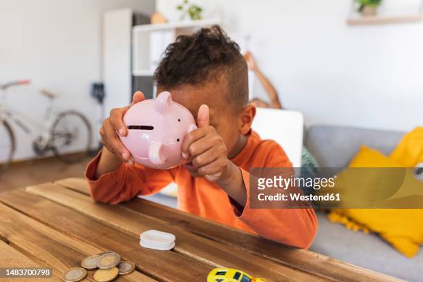 boy opening piggy bank to count coins at home - taschengeld kind stock-fotos und bilder