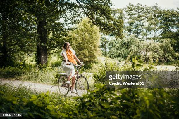 woman riding bicycle amidst trees - cycling woman stock-fotos und bilder