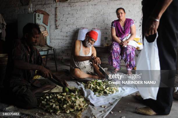 Indian labourers, who earn approximately 300 to 400 Indian rupees per day, cut raw mangoes which are used for pickles at a shop in Amritsar on July...