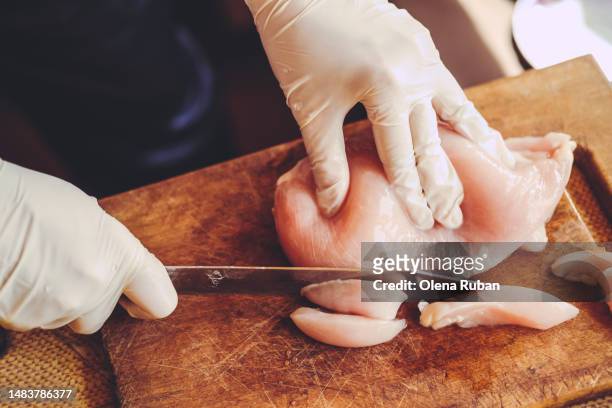 hands in gloves slicing raw chicken fillet. - chicken meat fotografías e imágenes de stock