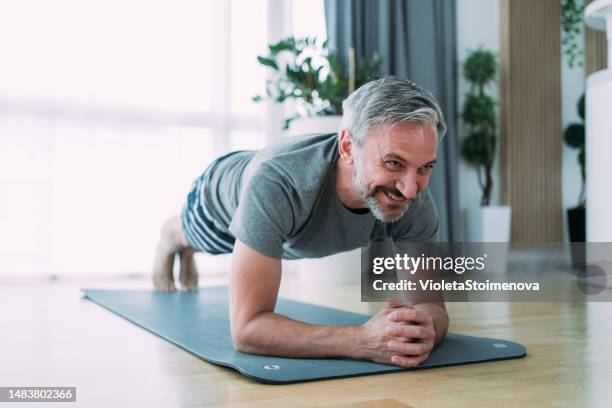 hombre maduro sonriente haciendo ejercicio en casa. - primer cuarto deportes fotografías e imágenes de stock