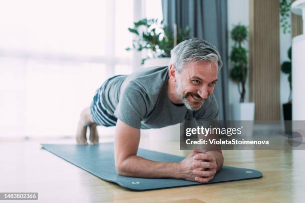 hombre maduro sonriente haciendo ejercicio en casa. - flexiones fotografías e imágenes de stock