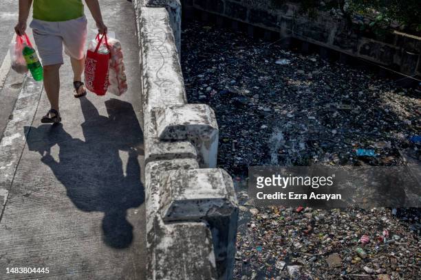 Woman carrying groceries walks above San Juan river, filled with plastic waste on April 20, 2023 in Manila, Philippines. The Philippines is the...