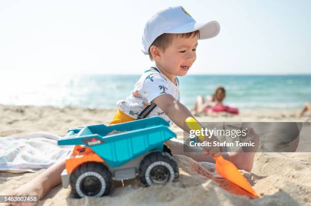 toddler playing on the beach sand with a toy truck by the seaside on a summer vacation - toy truck stock pictures, royalty-free photos & images