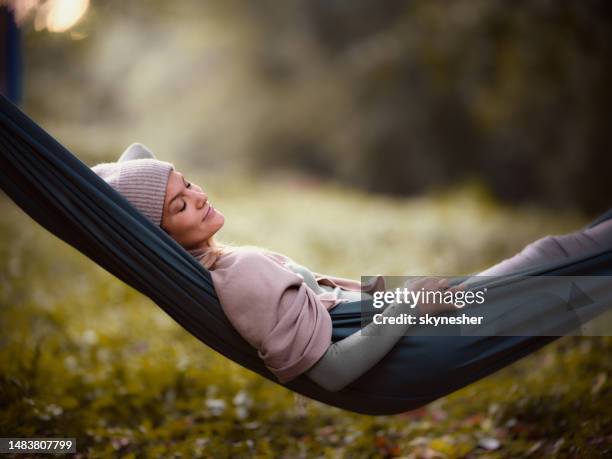 lächelnde frau, die sich in der hängematte im park entspannt. - hängematte stock-fotos und bilder