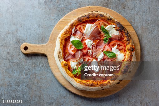Délicieuse pizza ronde avec prosciutto, mozzarella et basilic sur planche de bois Délicieuse pizza ronde avec prosciutto, mozzarella et basilic sur planche de bois