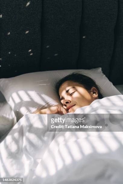 a beautiful young woman sleeps on white bedding in a hotel, light from the blinds on her face. - covers head with pillow stock-fotos und bilder