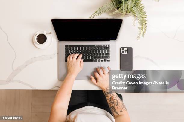 tattooed arms typing on a computer with espresso and phone - oberteil stock-fotos und bilder