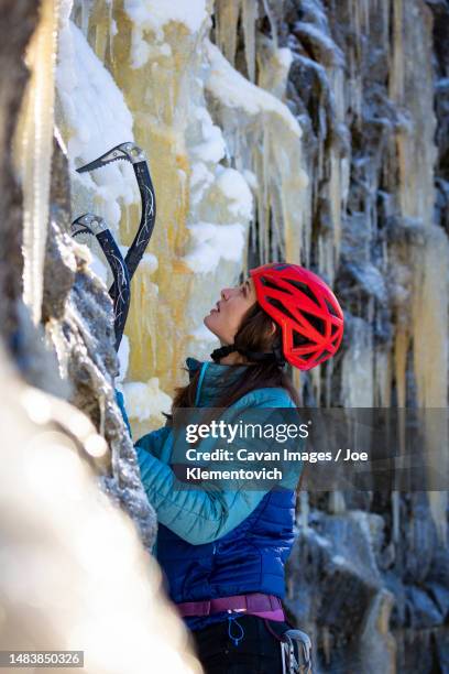 a woman in red helmet with long hair ice climbing - ice pick stockfoto's en -beelden
