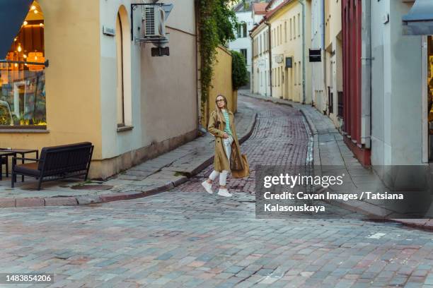 woman looks around as she walks down cobblestone street in old town - ビリニュス ストックフォトと画像