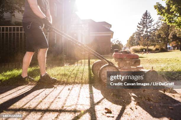 man mowing lawn with push mower at sunset - handgrasmaaier stockfoto's en -beelden