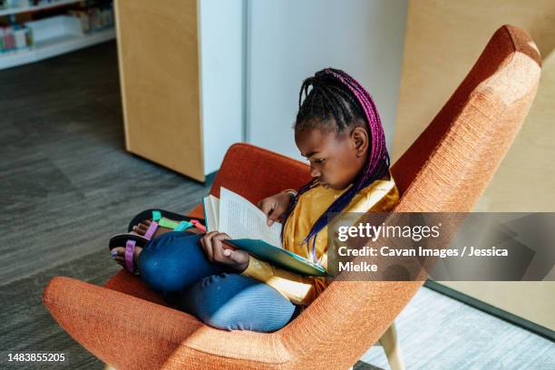 african american girl reading a book in a chair - public library stock pictures, royalty-free photos & images