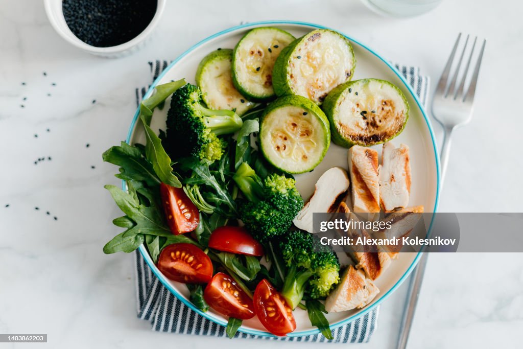 Grilled chicken meat and fresh vegetable tomato, broccoli, zucchini and arugula on plate in woman's hand. Organic balanced food