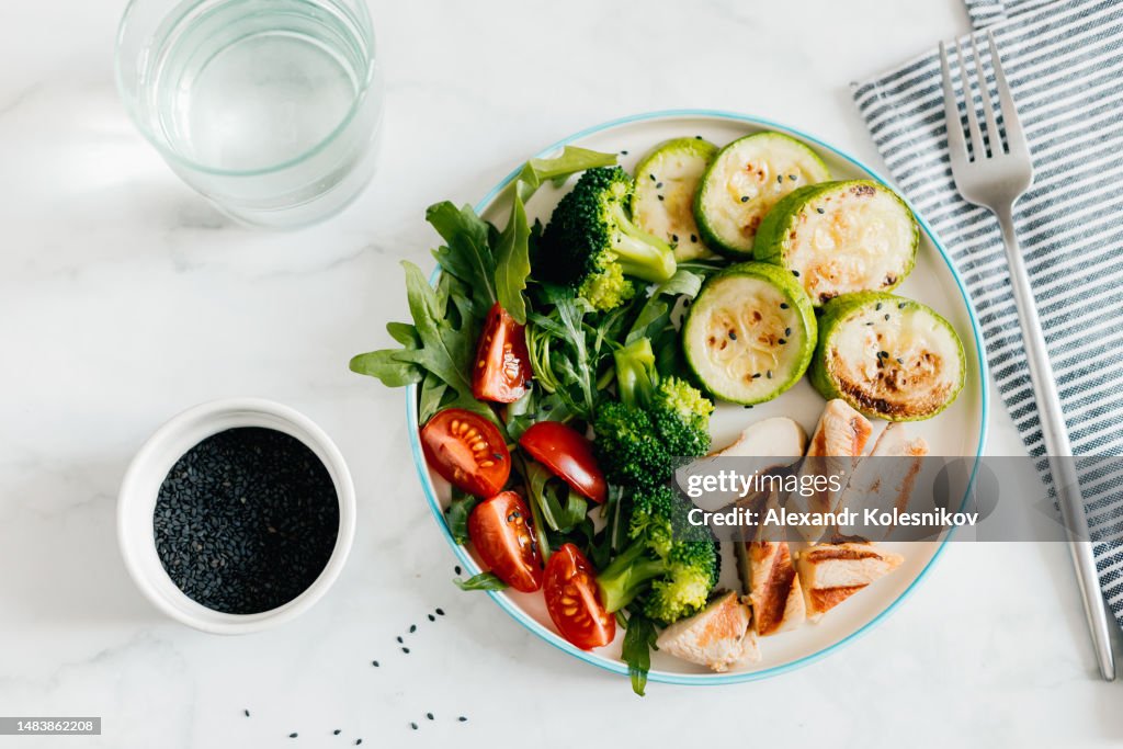 Grilled chicken meat and fresh vegetable tomato, broccoli, zucchini and arugula on plate in woman's hand. Organic balanced food
