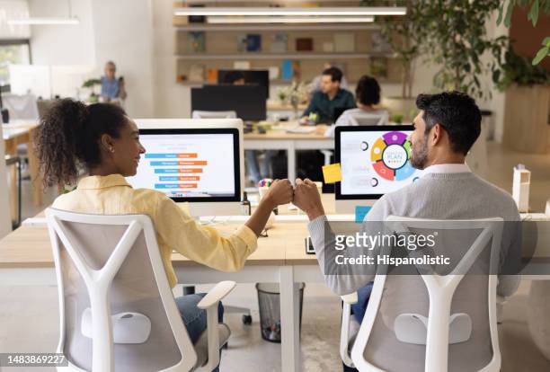 happy businesswoman giving a fist bump to her coworker at the office - employee engagement infographic stock pictures, royalty-free photos & images