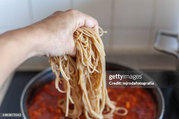 close-up of human hand grabbing a handful of spaghetti - wholegrain pasta stock pictures, royalty-free photos & images